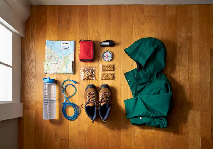 A flat lay of essential hiking gear for the Breakneck Ridge hike, including boots, a map, compass, and water.