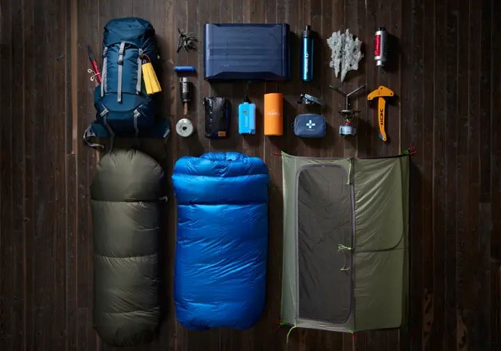 A complete set of backpacking gear for Glacier National Park, including a tent, backpack, sleeping bag, bear canister, and ice axe, laid out neatly on a wooden floor.