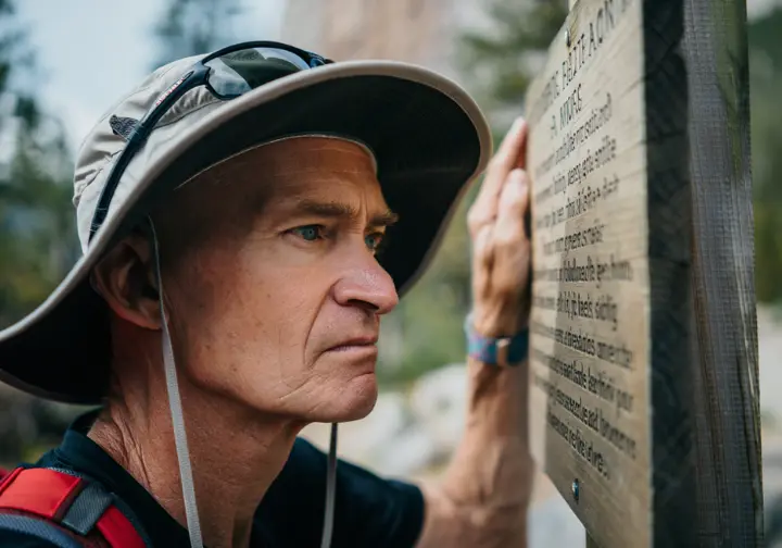 A hiker demonstrating trail intelligence by carefully reading a warning sign about difficulty before starting a hike at Mohonk.