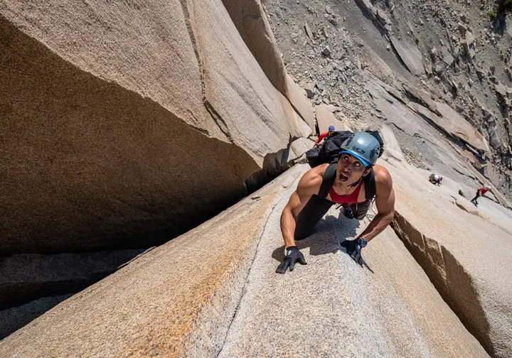 An experienced hiker wearing a helmet focuses intently while navigating a steep and exposed rock scramble on a strenuous Colorado mountain trail.
