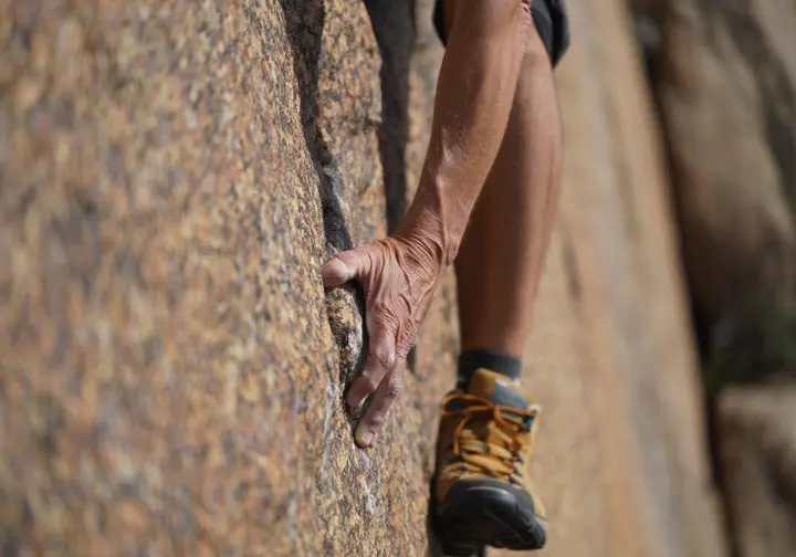 Close-up of a hiker's hand and foot demonstrating the three-points-of-contact safety rule while rock scrambling.