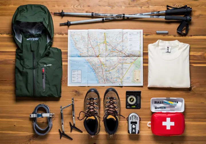 A flat lay of essential hiking and safety gear including boots, a map, compass, and microspikes.