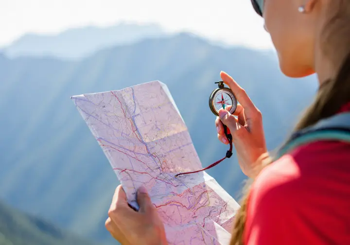 A hiker skillfully uses a map and compass to navigate in the mountains, demonstrating essential backcountry competence.