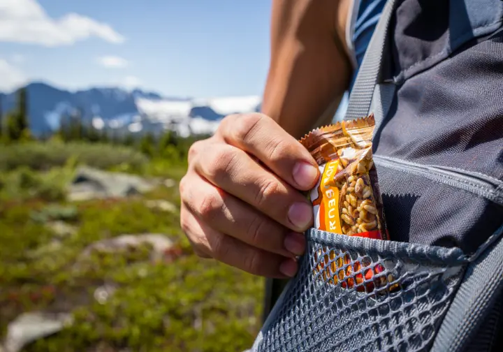 A hiker practices responsible Leave No Trace principles by picking up a piece of litter and packing it out, with a fragile alpine tundra landscape in the background.