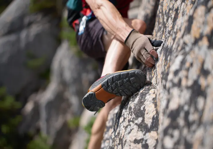 A close-up of a hiker demonstrating proper rock scrambling safety by maintaining three points of contact on a rock face.