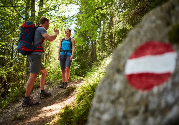 Two hikers greeting each other respectfully on a trail in Slovenia, with a Knafelc blaze trail marker visible.