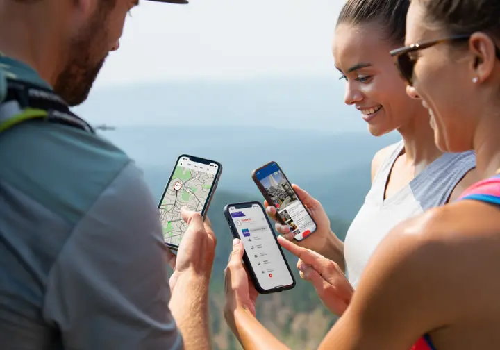 Three diverse hikers on a scenic overlook share and compare the different apps on their smartphones, representing final recommendations for different hiker toolkits.