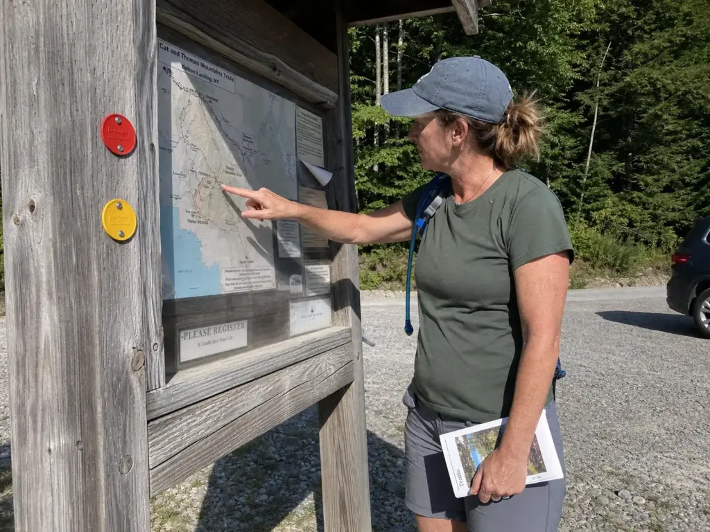 Hiker checking a trailhead map board before starting a Lake George hiking trail