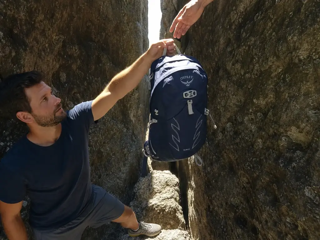 Hiker passing a small Osprey daypack through the narrow Lemon Squeeze crevice at Mohonk