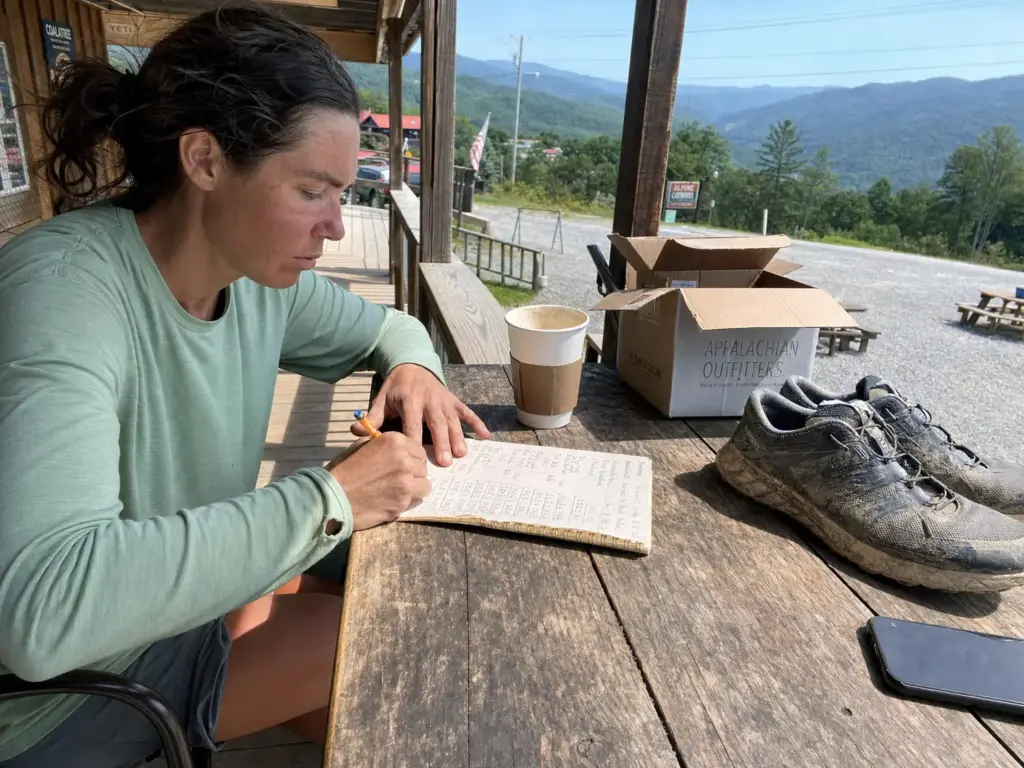 Hiker doing shoe replacement math in a notebook on a trail town hostel porch