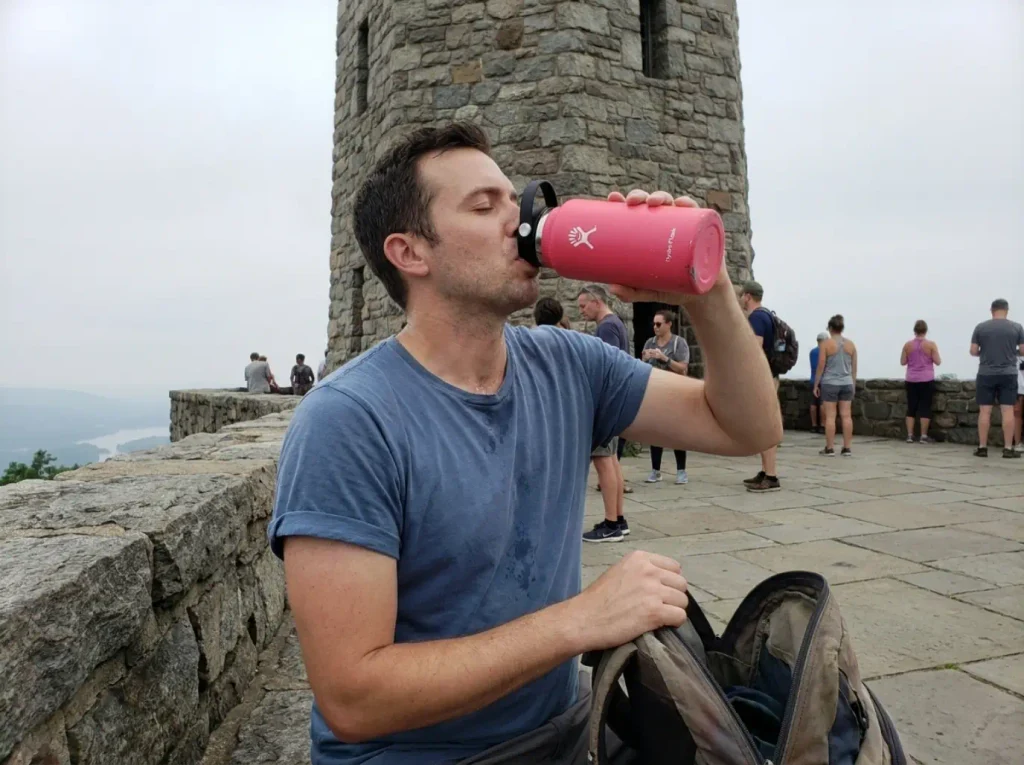 Hiker drinking from a Hydro Flask bottle at the Perkins Memorial Tower summit on Bear Mountain