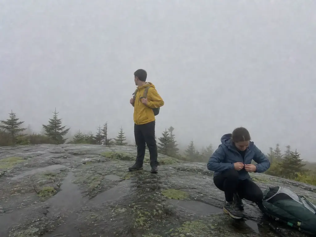 Hikers stopped on a fogged-in ridge on a Lake George hiking trail with no summit view