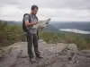 Hikes in North Jersey Sorted by What You Want Hiker checking a paper trail map at a rocky Highlands overlook on a North Jersey hike