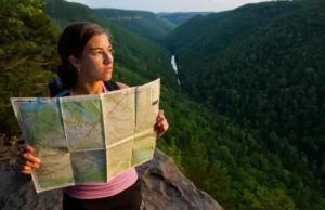Beyond the List: A Hiker’s Analysis of Central PA A hiker studies a topographic map at a scenic overlook in Central Pennsylvania during golden hour, with rolling, forested ridges stretching into the distance.