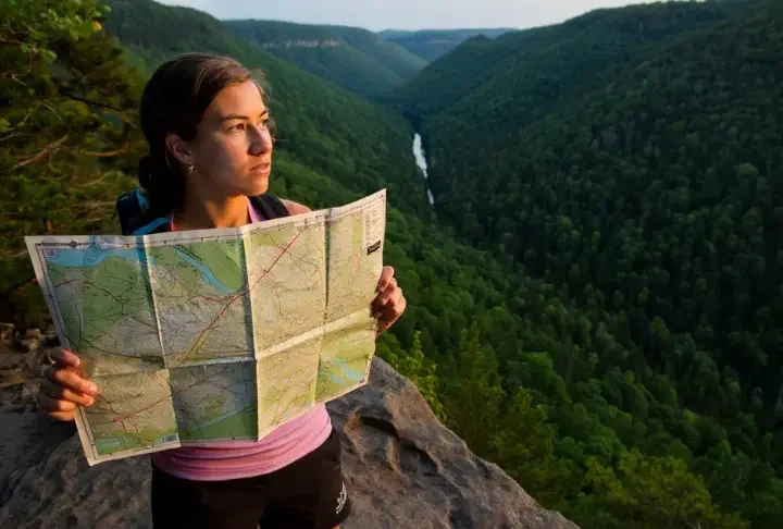 A hiker studies a topographic map at a scenic overlook in Central Pennsylvania during golden hour, with rolling, forested ridges stretching into the distance.