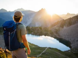 A backpacker overlooks a spectacular Colorado mountain range with an alpine lake at sunrise, about to start a backpacking loop.
