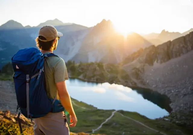 A backpacker overlooks a spectacular Colorado mountain range with an alpine lake at sunrise, about to start a backpacking loop.