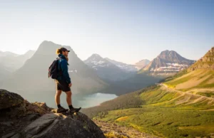 Glacier NP Day Hikes: A Field-Tested Planning Guide A hiker stands on a scenic overlook on the Highline Trail, thoughtfully planning their route while looking out over the mountains and valleys of Glacier National Park at sunset.