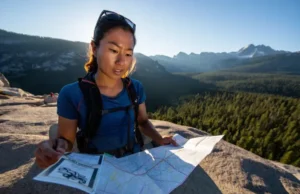 NorCal Backpacking Planner: A Comprehensive Guide to Trails, Permits, and Skills A female hiker stands on a granite ridge overlooking a vast Northern California landscape, carefully planning her route using a map and permit.