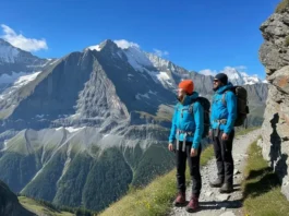 A full-body shot of two hikers on a narrow trail in the Swiss Alps, looking at the view of the Eiger mountain.