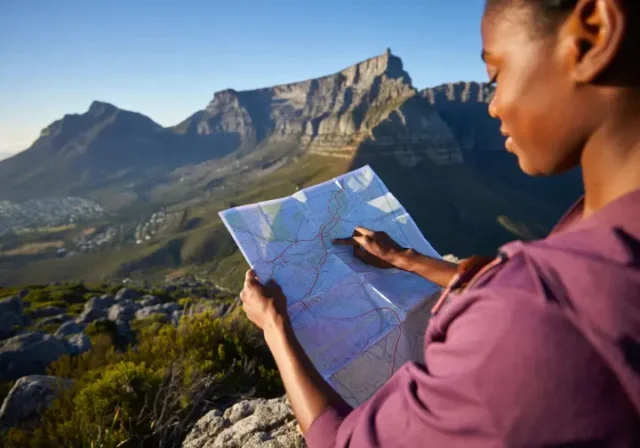00 table-mountain-hiker-planning-guide A hiker studies a map while looking out at the full expanse of Table Mountain, planning a data-backed hiking adventure.