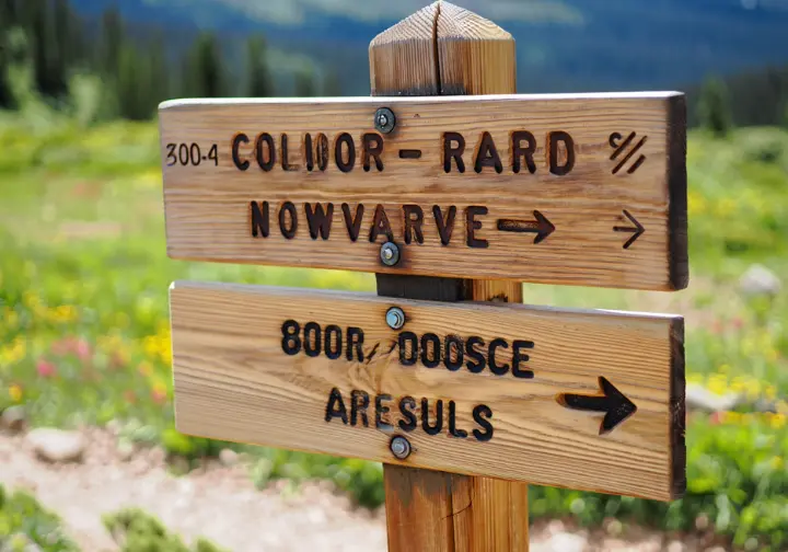 A wooden trail sign at a junction in the Colorado mountains, representing the choice between different backpacking loops for various skill levels.