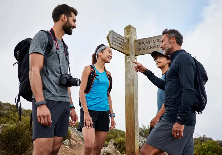 A diverse group of hikers representing different styles pauses at a trail fork, illustrating how to find the perfect trail for your hiking style.