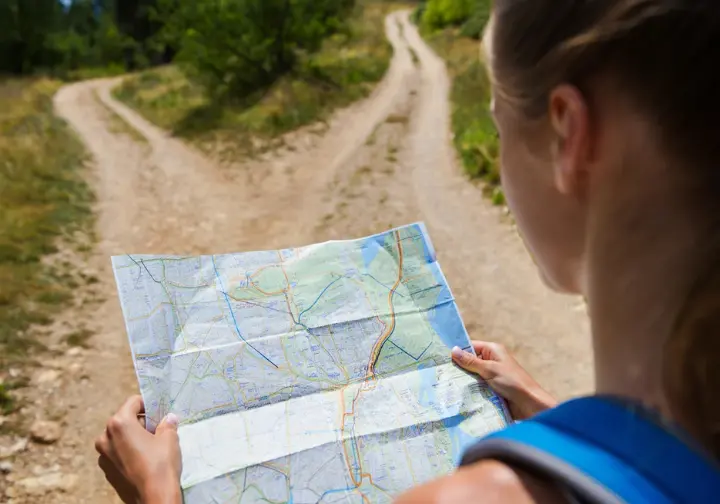 A close-up of a hiker's hands holding a map at a fork in the trail, illustrating the process of choosing the right path based on data.