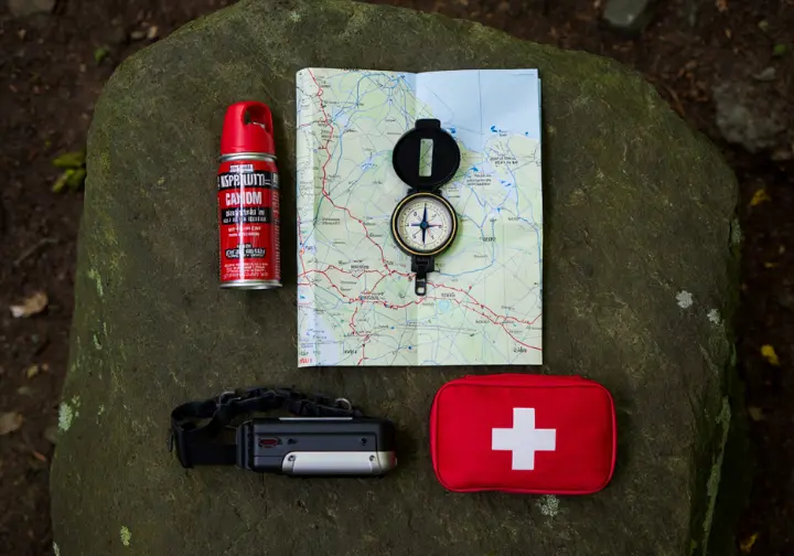 A flat lay of essential hiking safety gear on a rock, including bear spray, a map and compass, a first-aid kit, and a headlamp, illustrating how to stay safe and prepared in Glacier.