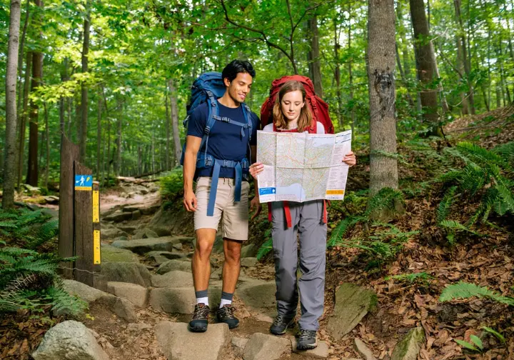 Two hikers navigating a rocky, forested trail using a map while hiking in Sterling Forest State Park NY.