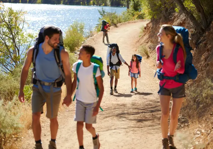 Hikers of different skill levels, including a family and a backpacker, enjoy a sunny day on a scenic trail alongside a lake in Land Between the Lakes.