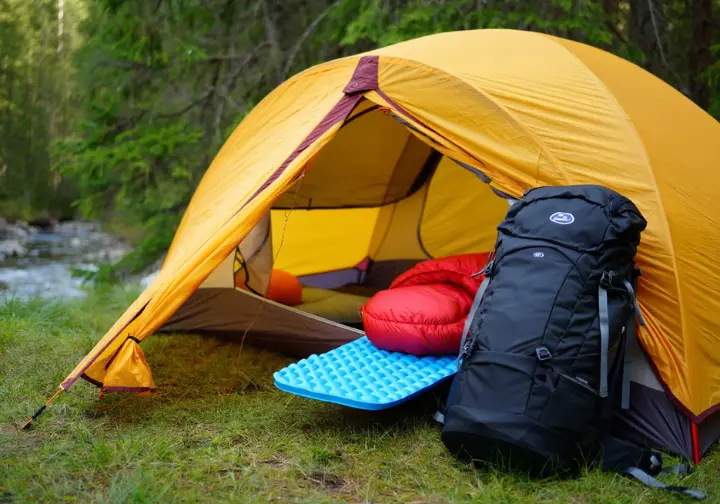 A detailed view of the core overnight hiking systems, showing a pitched tent, a backpack, and a sleep system at a campsite.