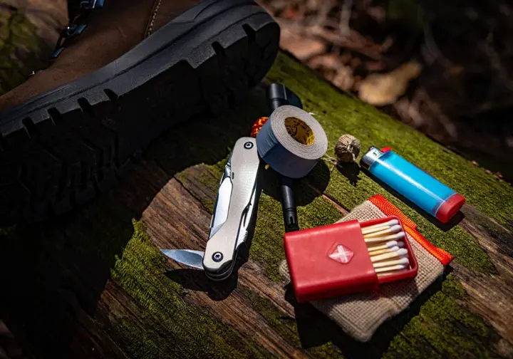 Essential hiking tools for safety and repair laid out: multi-tool, duct tape, fire starter kit, and hiking boot sole.