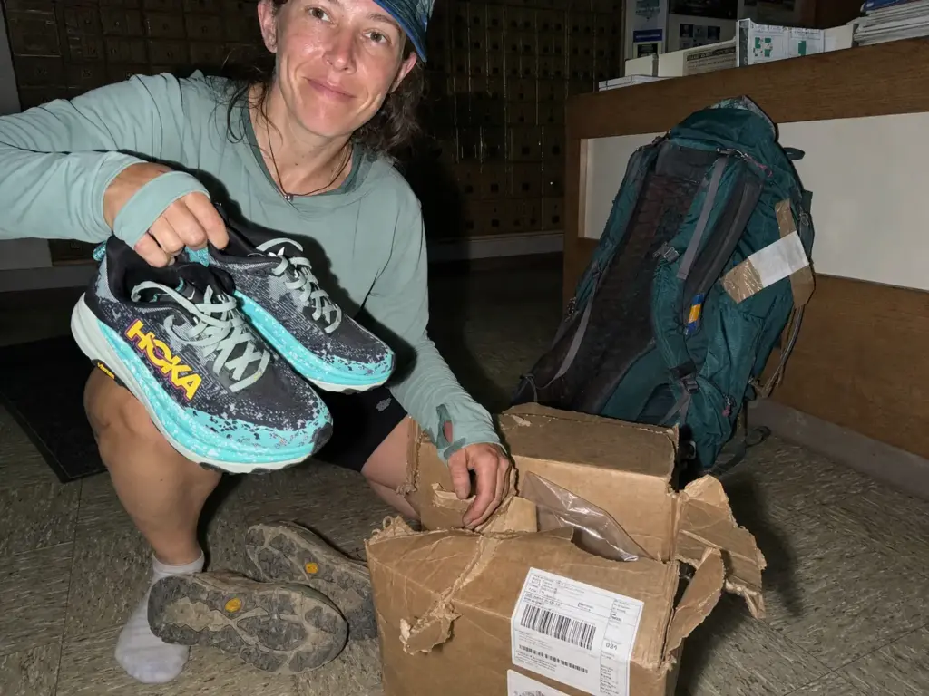Hiker swapping worn trail runners for a fresh pair from a send-ahead box in a trail town