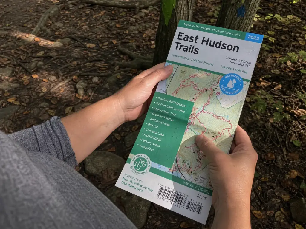 Hands holding a NY-NJ Trail Conference East Hudson trail map at a blazed junction in Fahnestock