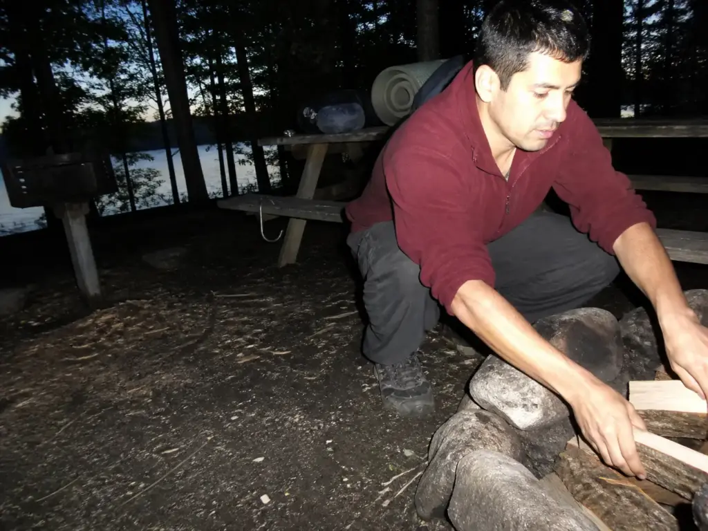 Camper sorting gear at a fire ring near Canopus Lake in Fahnestock State Park at dusk