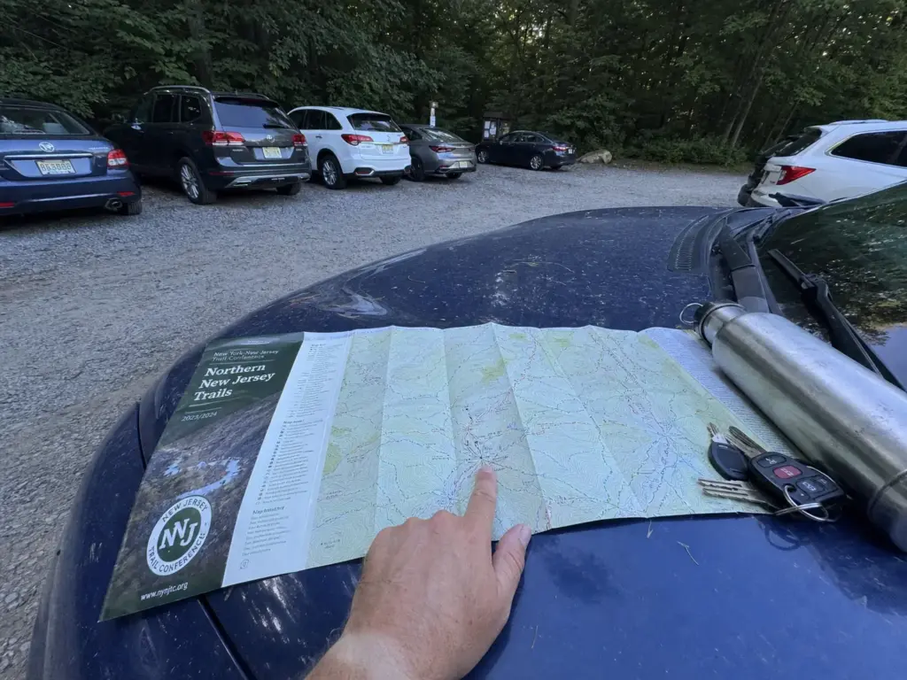 Paper trail map on a car hood at a full North Jersey trailhead parking lot