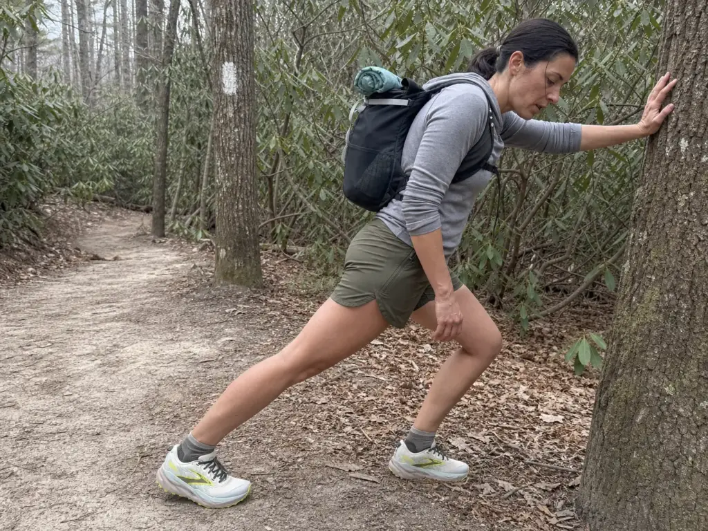 Hiker stretching her calf on a trail during the transition from hiking boots to trail runners