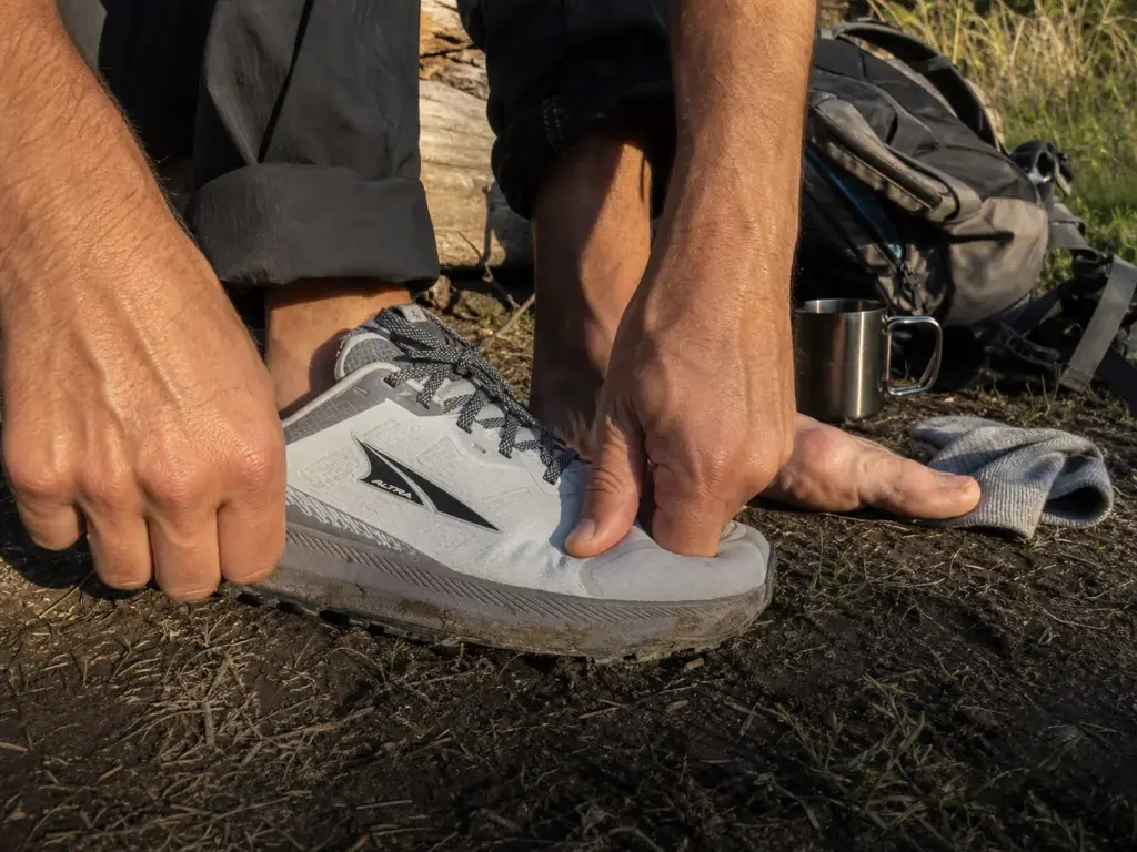 Hands checking a thumb's width of toe box space in an Altra trail runner after a day of hiking