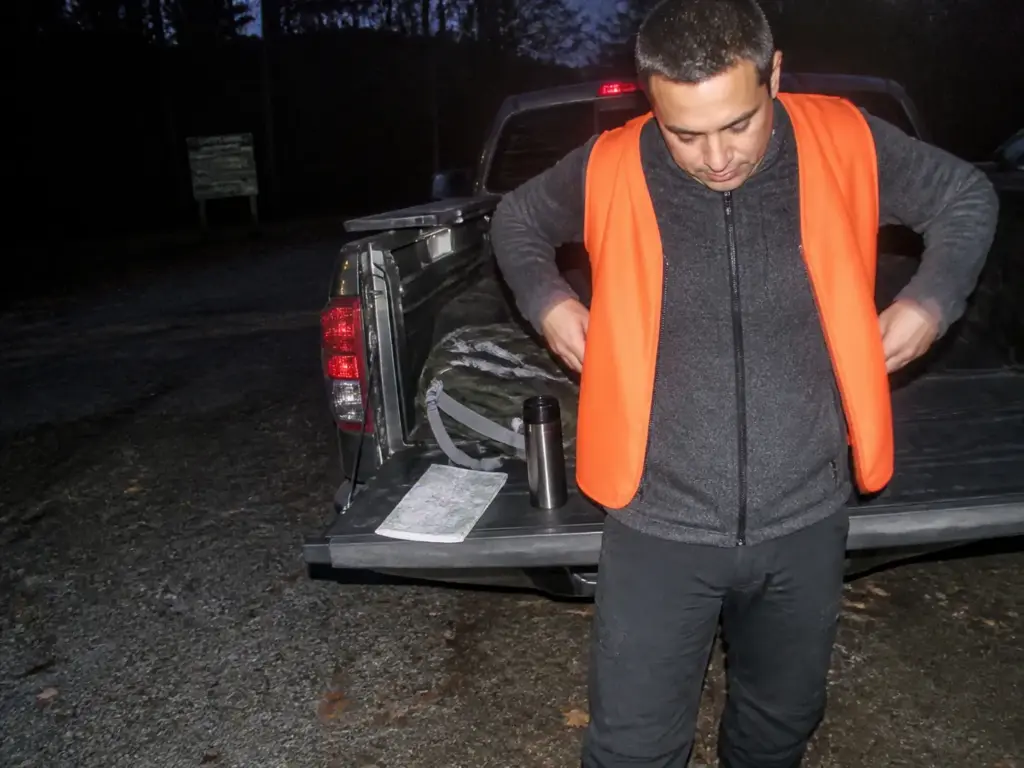 Hiker pulling on a blaze orange safety vest at a Sterling Forest trailhead in hunting season