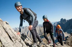 The Non-negotiable Gear for Alpine Scrambling Three alpine scramblers with essential gear ascend a rocky mountain ridge under a clear sky, illustrating non-negotiable equipment for essential gear for alpine scrambling and easy mountaineering.