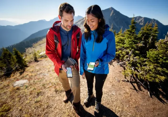 Two hikers on a mountain trail comparing different hiking GPS apps on their smartphones, representing the best hiking apps of 2025.