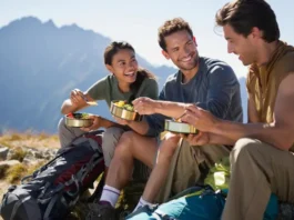 Three diverse hikers enjoying a delicious, easy-to-prepare meal on a mountain ridge, showcasing effective backpacking food and meal planning.