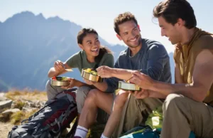 Beyond Granola: Easy & Delicious Trail Recipes Three diverse hikers enjoying a delicious, easy-to-prepare meal on a mountain ridge, showcasing effective backpacking food and meal planning.
