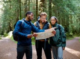 Three hikers, appearing lost, consult a map on a forested trail, embodying a hiking emergency.