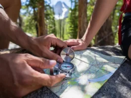 Hands using a compass and topographic map in a forest, emphasizing mastery of analog navigation skills for hikers.