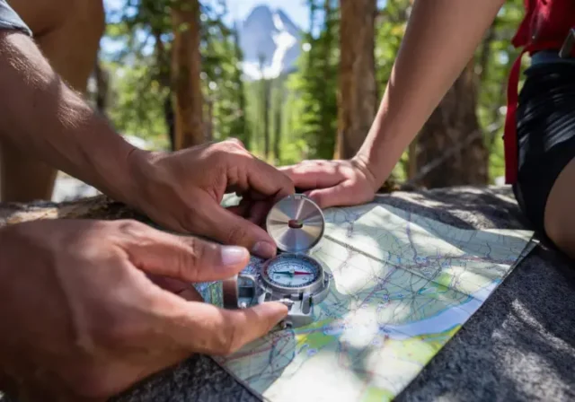 Hands using a compass and topographic map in a forest, emphasizing mastery of analog navigation skills for hikers.