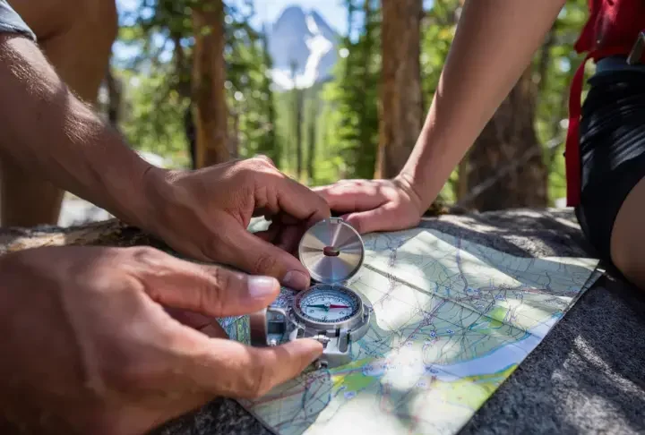 Hands using a compass and topographic map in a forest, emphasizing mastery of analog navigation skills for hikers.