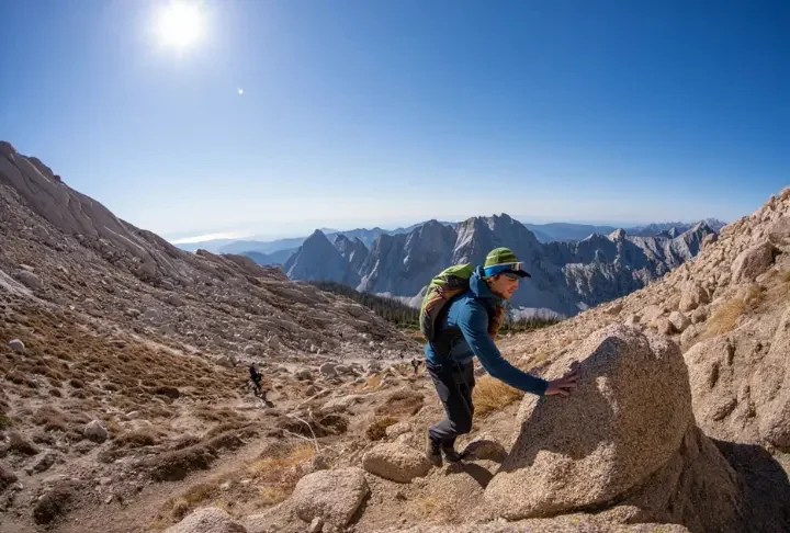 A hiker transitions from a trail to a rocky incline, illustrating the concept of alpine scrambling and bridging the gap between hiking and climbing.