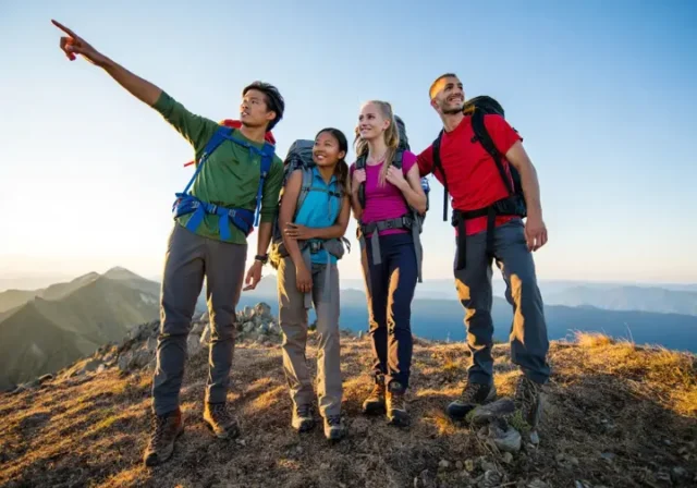 Four diverse thru-hikers stand on a mountain summit at golden hour, overlooking vast peaks, embodying the mind, body, and budget preparation for a long-distance trail.